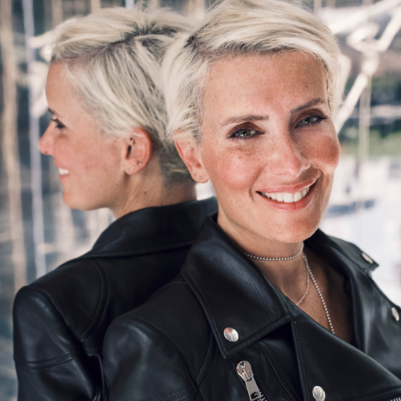 Cecilia Taieb, leaning her back against the mirror, and smiling with a black leather jacket.
