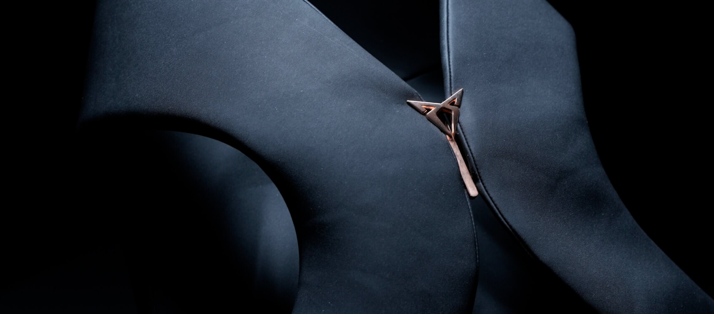 A close-up shot of dark fabric garment with a unique metal fastener, against a dark background.
