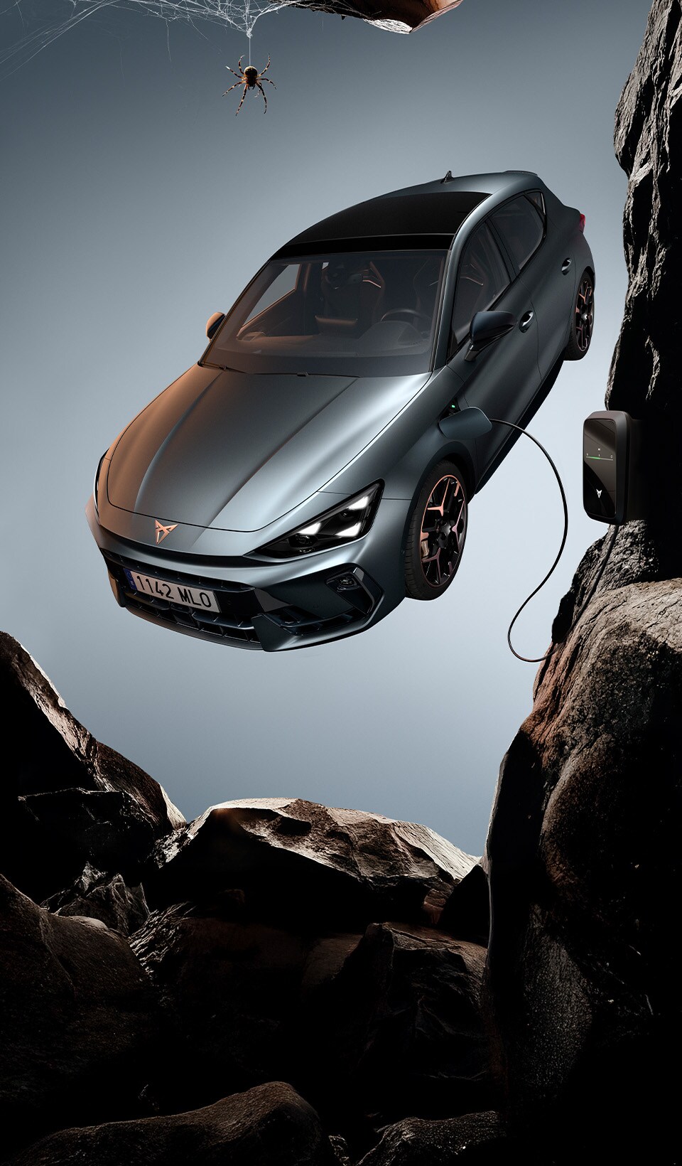 A CUPRA Leon hatchback seen from an elevated angle with its headlights on, next to a person covered in dark, flowing fabric that drapes onto the ground.